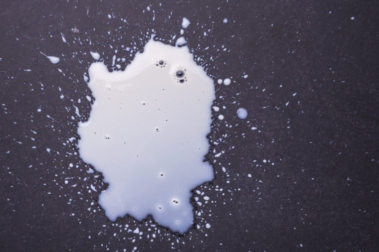 White milk spilled and splash on the dark floor surface. Top view