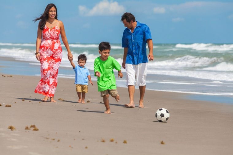 A happy family of mother, father parents & two boy son children, playng football or soccer and having fun in the sand of a sunny beach