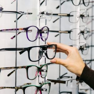 Eyeglasses shop. Stand with glasses in the store of optics. Woman's hand chooses glasses.