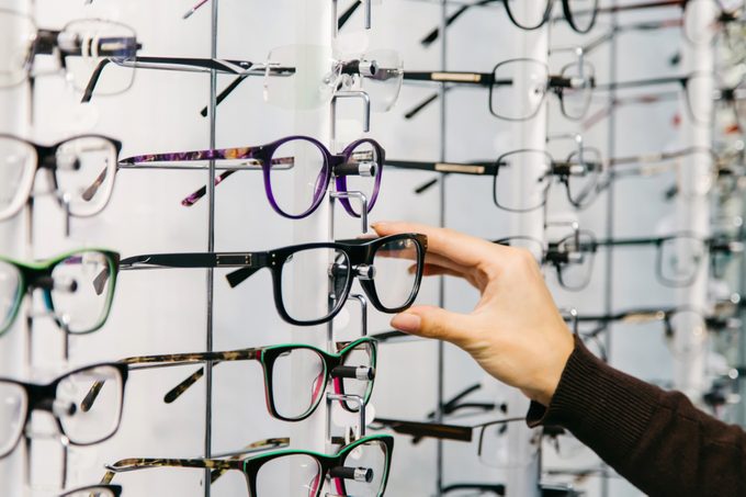Eyeglasses shop. Stand with glasses in the store of optics. Woman's hand chooses glasses.