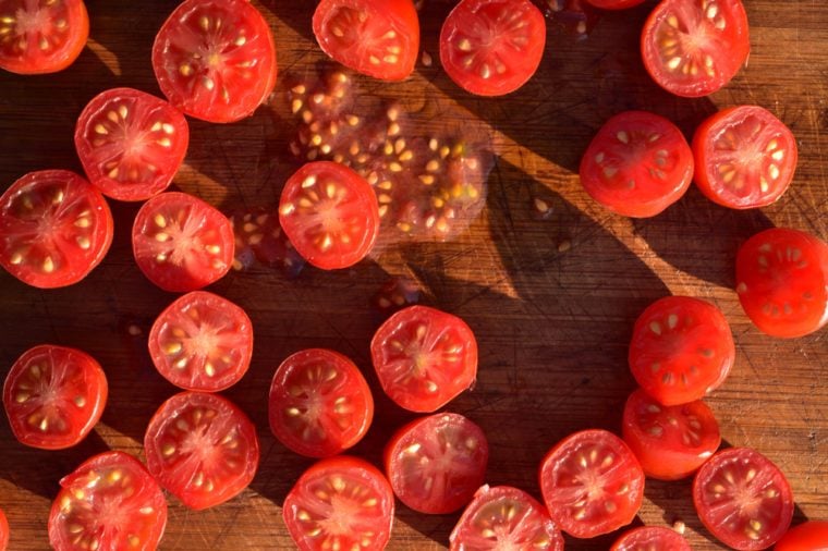 above view of grape tomatoes cut into halves on wood cutting board