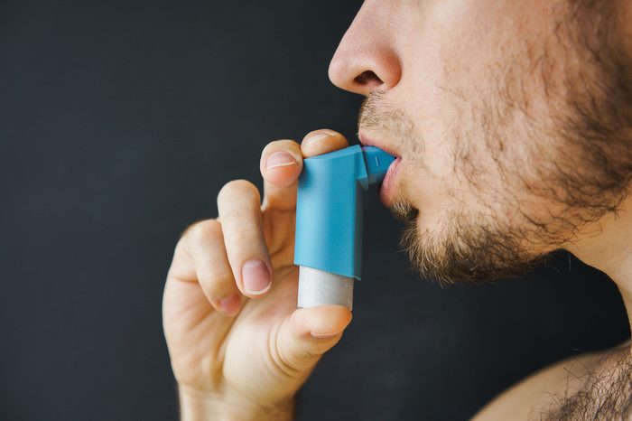 male asthmatic with an aerosol inhaler in his hand takes a breath.