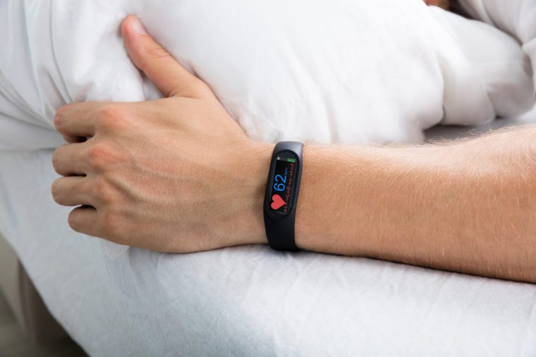 Fitness Activity Tracker With Heartbeat Rate On Man's Hand Over Bed
