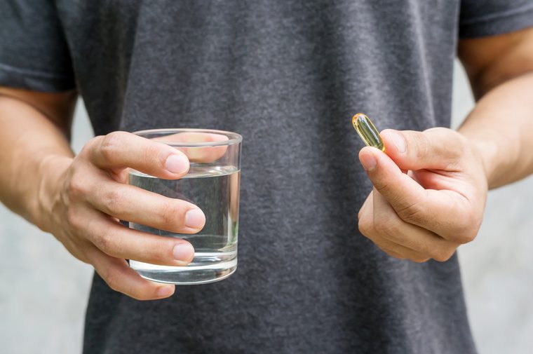 Close up of a man holding a fish oil capsule and a glass of water.