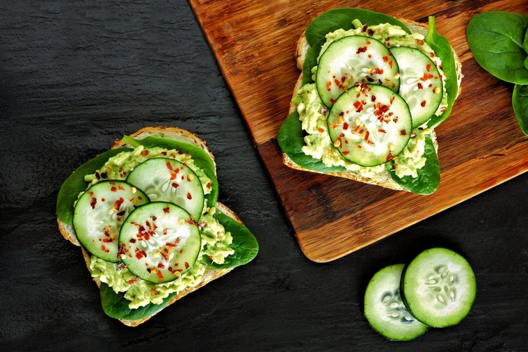 Two avocado toast sandwiches with cucumber and spinach on whole grain bread