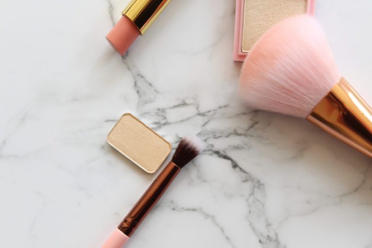 Gold and pink makeup objects against white marble copy space.