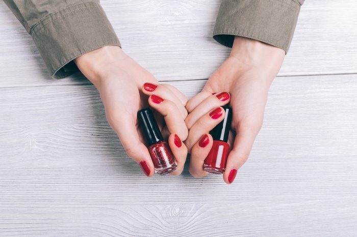 Bottles with red nail polish in female hands top view