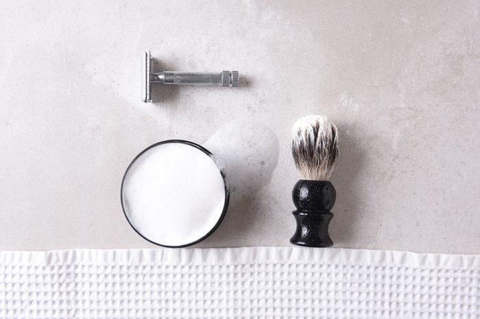 Shaving Still Life: Safety razor with towel, brush and soap on a gray tile surface.