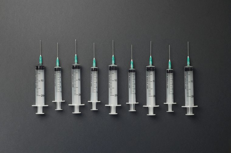 Syringes organized in a row over dark grey background, top view