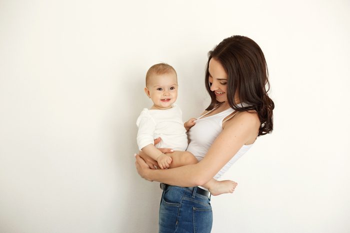 Young beautiful happy mother smiling laughing holding her baby daughter over white wall.