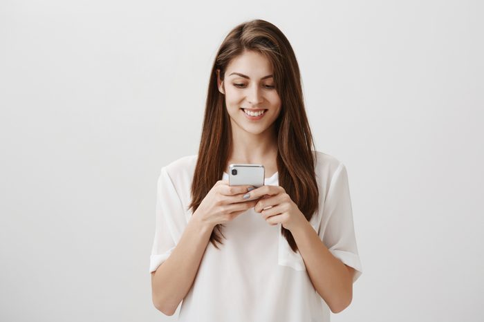 Popular attractive caucasian female student holding smartphone, looking at screen with excitement, typing answer or reading feedback about new project