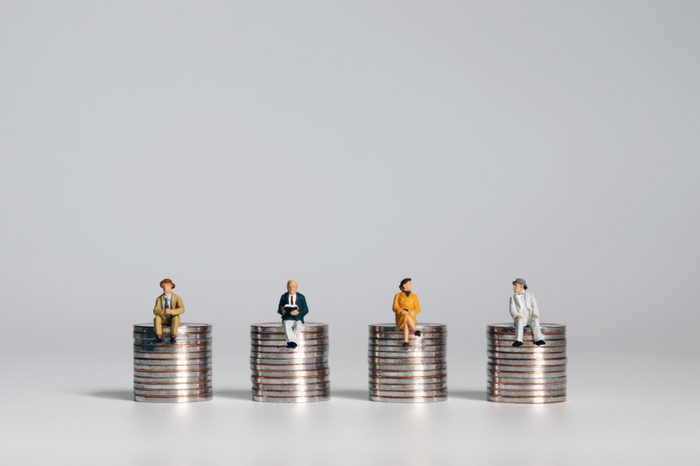 Miniature people sitting on piles of coins. A concept about social costs.
