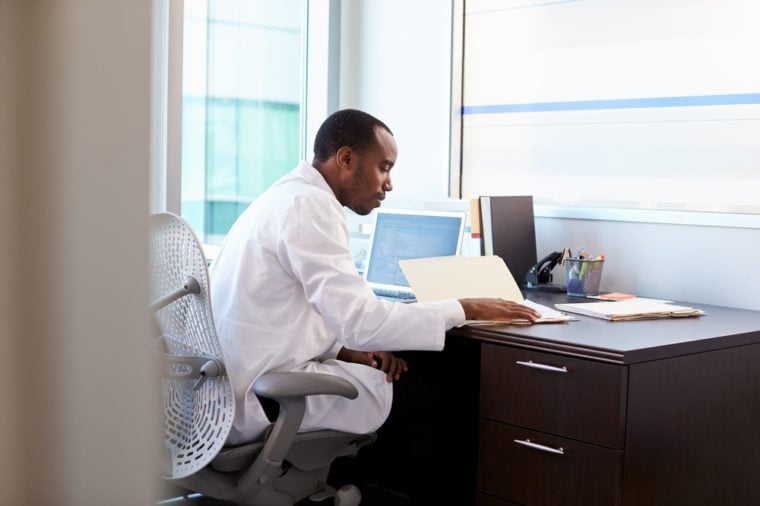 Doctor Wearing White Coat Reading Notes In Office