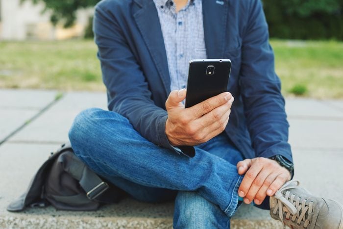 Young casual man using smart phone sitting outdoor