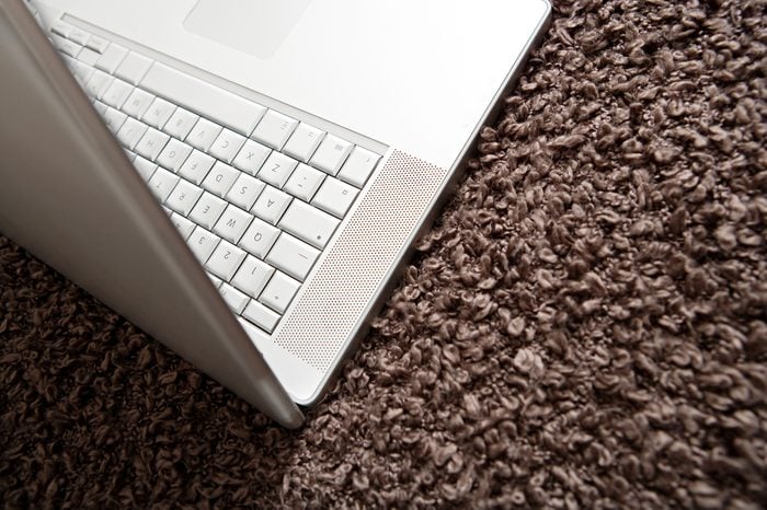 Over head view of a silver open laptop computer lying on a woolly brown blanket in a hotel room. Technology still life object with no people, interior.