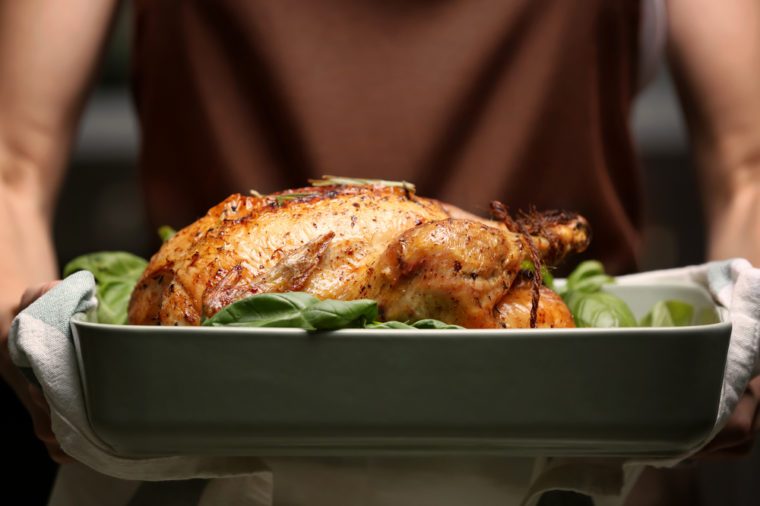 Woman holding baking dish with golden roasted turkey