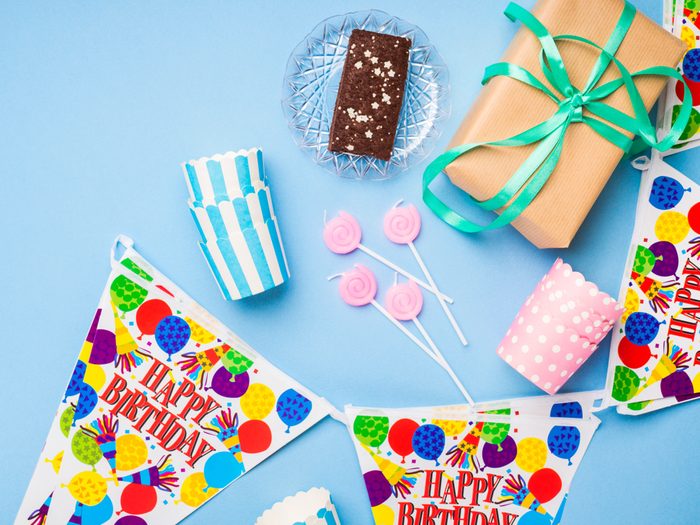 Happy Birthday party items flat lay. Candles, gift box, decoration banner, paper glasses, chocolate cake