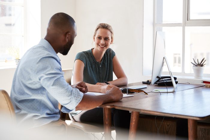 Man and woman sitting at a desk talking in an office smiling