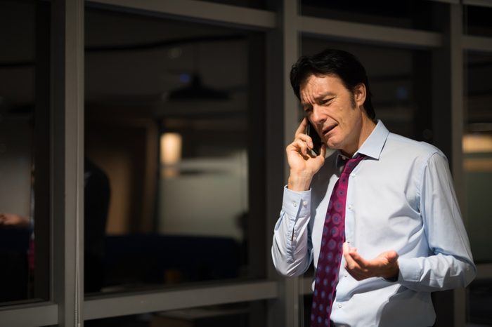 Mature Businessman In Office At Night Talking On Mobile Phone