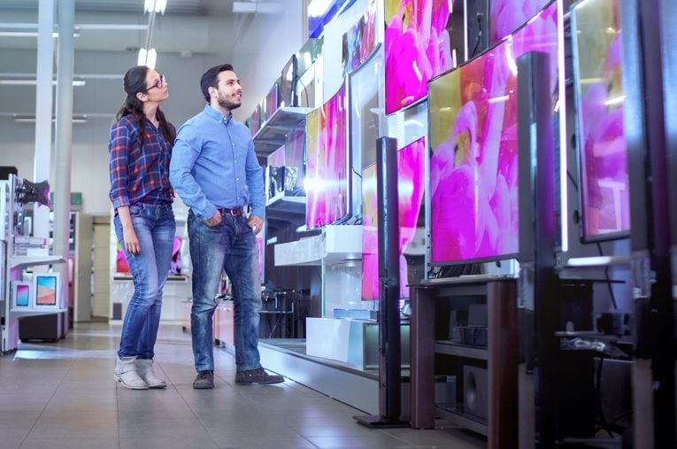 In the Electronics Store Young Couple is Choosing Which a New Model of 4K TV's is Best for Their Home and Budget.