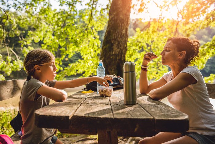 Mother and daughter eating healthy snack at a picnic table in the forest