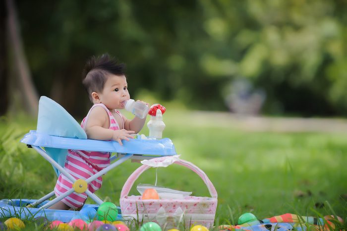 Cute baby drinking milk from a bottle in a baby walker, happily and relaxes in the garden,Important part of the family.