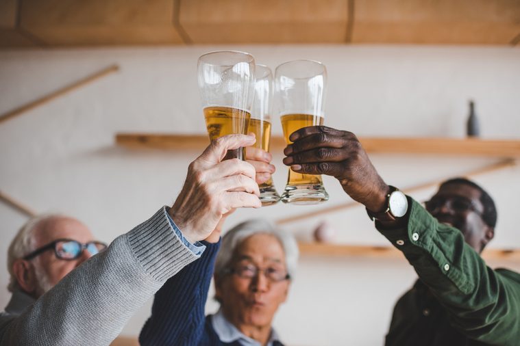 group of senior friends clinking glasses of beer at bar
