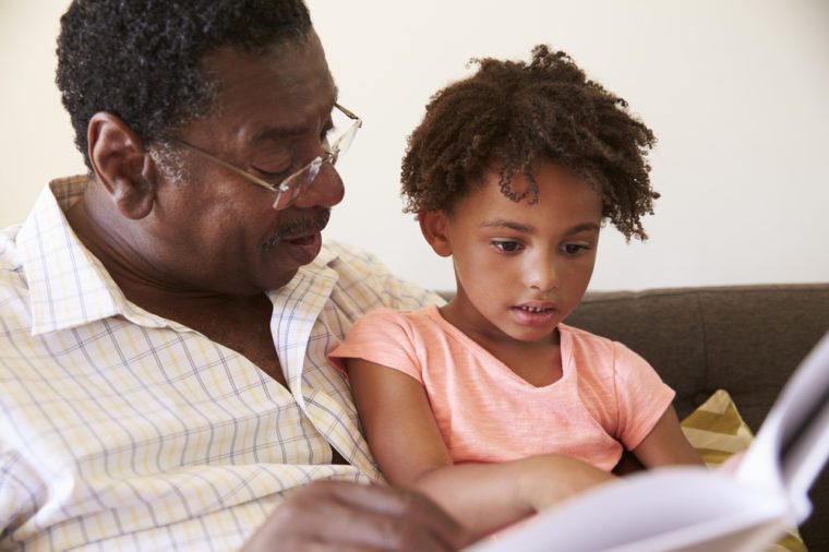Grandfather And Granddaughter Reading Book At Home Together