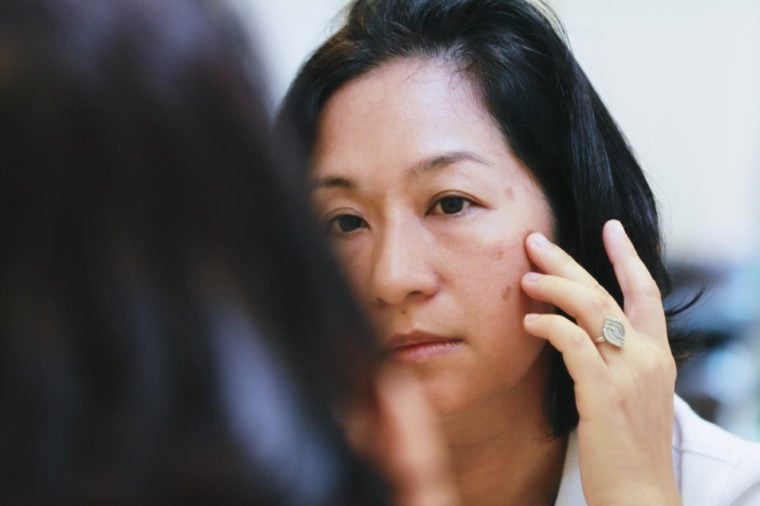 40s Asian woman looking on her face skin in the mirror and look worried or concern about the Aging skin problem.Brownish colored patches or melasma appear on the cheeks.