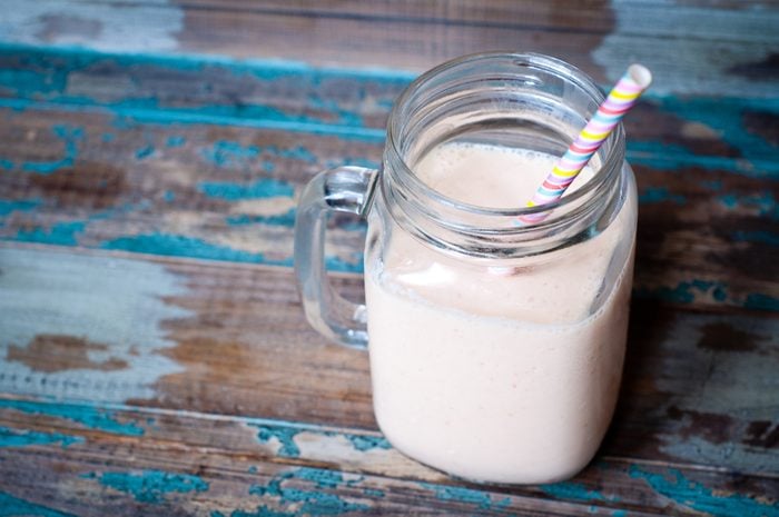 Smoothie milkshake made from peach,melon and papaya blended with kefir yogurt. Served in a jug style glass on a rustic wooden table with a colorful stripy straw.