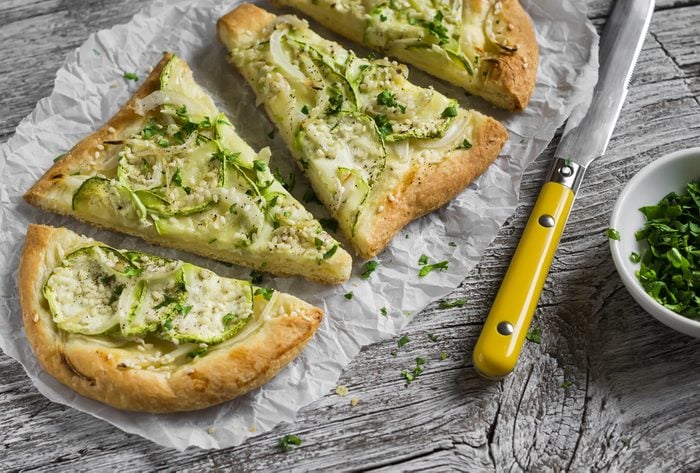 pizza with zucchini, onion, cheese and sesame seeds on a light wooden background