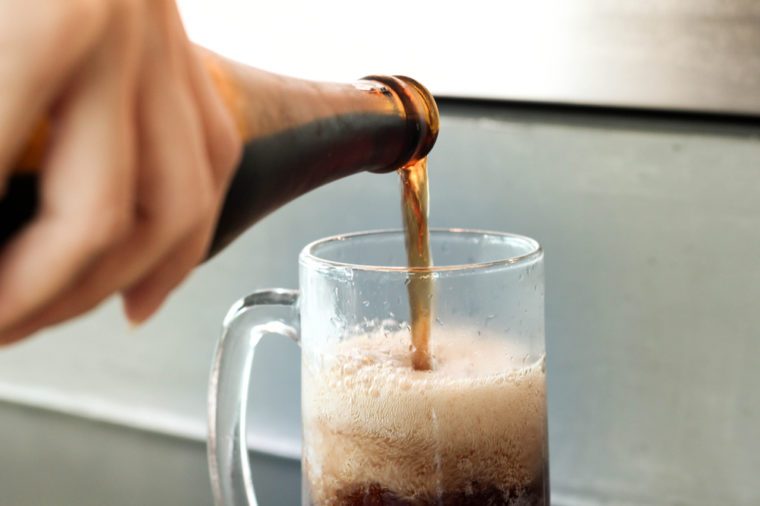 hand hold and pour root beer to glass , ice cola