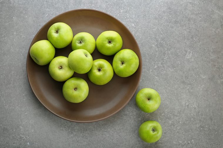 Plate with fresh green apples on grey background