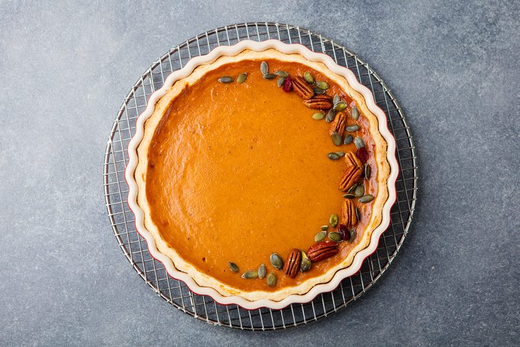 Tasty pumpkin pie, tart made for Thanksgiving day in a baking dish on a colling rack. Grey stone background. Top view.