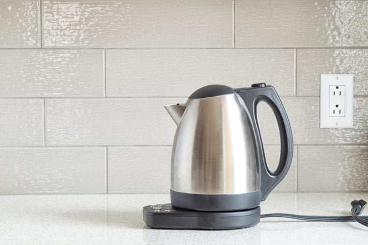 Electric stainless steel kettle on a granite counter top against a ceramic background