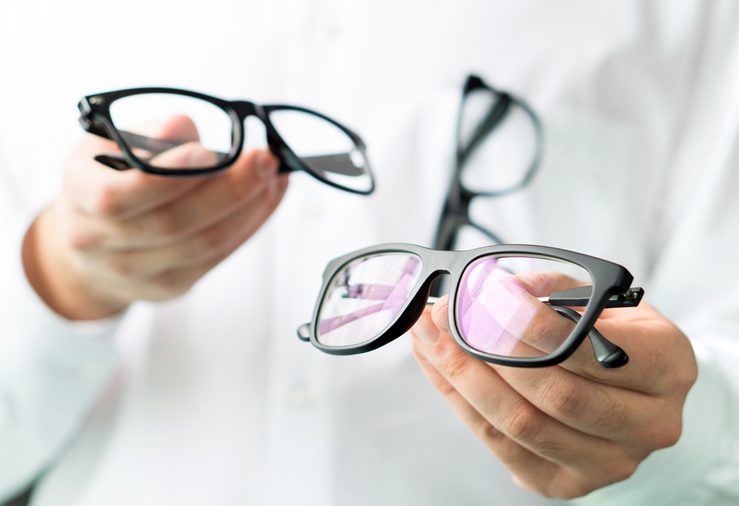 Optician comparing lenses or showing customer different options in spectacles. Eye doctor showing new glasses. Professional optometrist in white coat with many eyeglasses.
