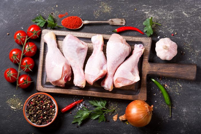 fresh chicken legs on wooden board with ingredients for cooking, top view
