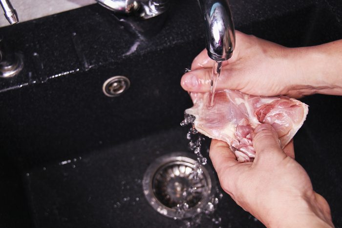 Man's hands washing and cleaning chicken wings at the kitchen sink