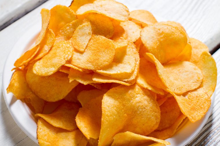 Potato chips on a plate. White plate with yellow chips. Fast snack at new diner. Good example of processed food.