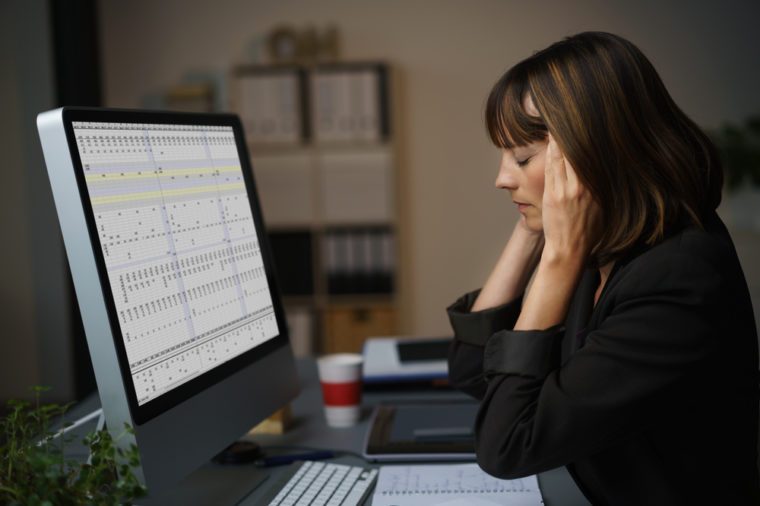 Side View of a Tired Businesswoman Working on her Computer at her Table, Holding her Head with Eyes Closed.