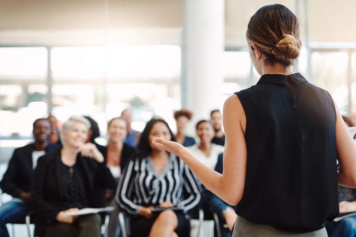 Shot from behind of a young businesswoman delivering a speech during a conference