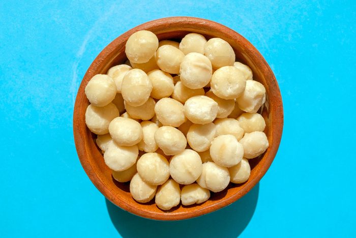 Lots of Macadamia nuts in a brown bowl on blue background.