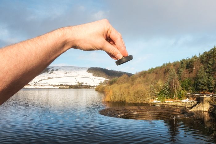 Human hand holding a sink plug, appearing to be pulled from a lake at Ladybower reservoir spillway.