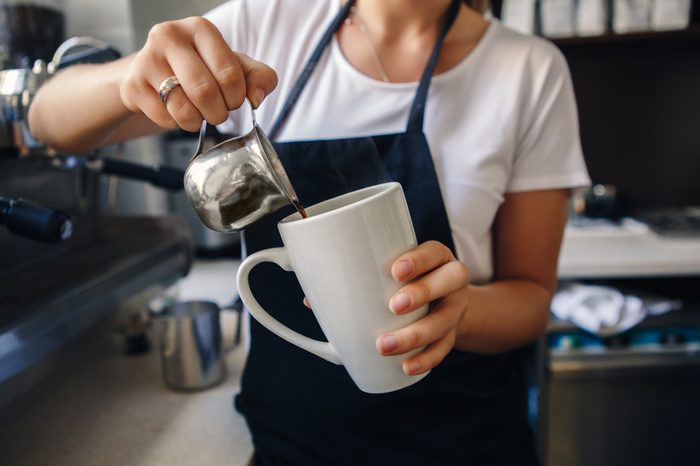 Closeup macro shot of Caucasian woman hands making coffee. Barista pouring hot coffee in white mug cup