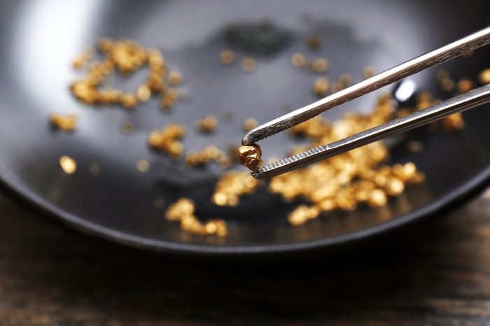 Tweezers holding Gold nugget grain, on black background, close-up