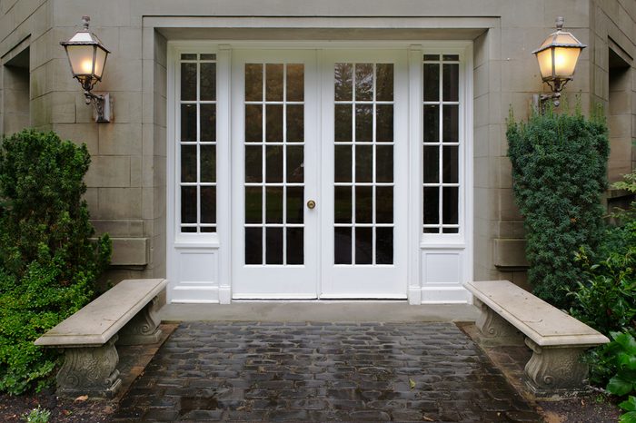 Elegant stone walkway bordered by stone benches leading to a double glass paned front door with two large front lanterns