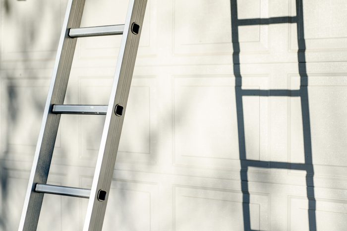 Aluminum ladder leaning against white garage door, with strong shadow and warm natural sun light