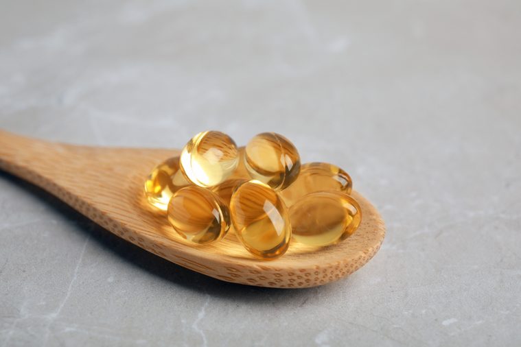 Spoon with cod liver oil pills on table, closeup