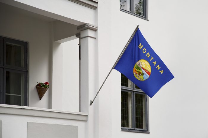 Montana flag. Montana state flag hanging on a pole in front of the house. State flag waving on a home displaying on a pole on a front door of a building. Flag raised at a full staff.