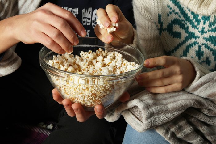 Young people watch movies and eating popcorn with a glass bowl, close-up